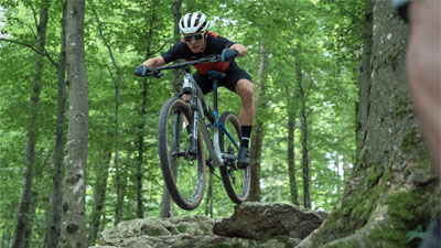 Ein Radfahrer fährt durch den Wald und springt gerade von einem Stein ab.