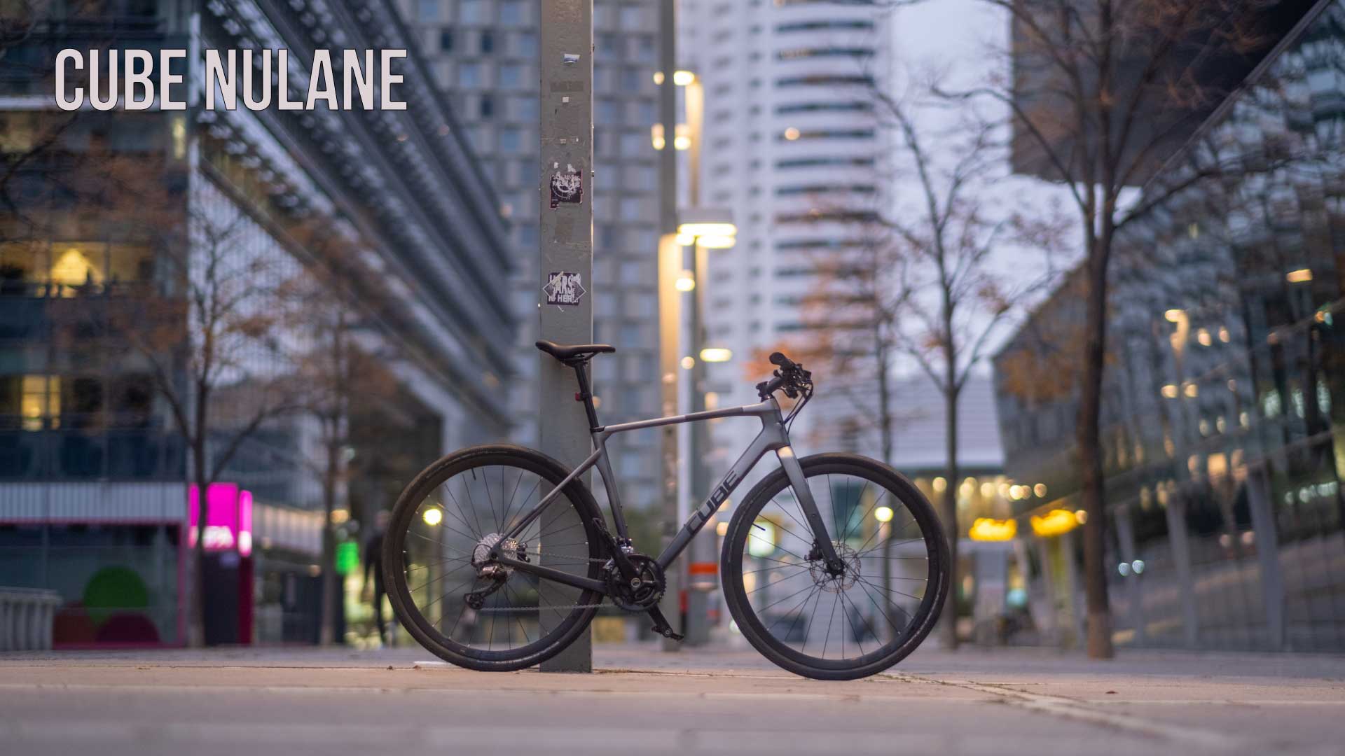 Banner mit der Aufschrift „Cube Nulane“. Ein Cube Nulane Fitnessrad lehnt an einer Säule im Stadtzentrum.