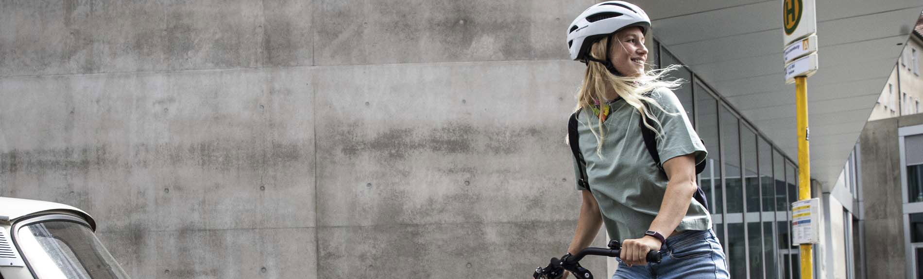 Eine Frau mit einem Fahrradhelm schaut nach rechts. Im Hintergrund ist eine graue Wand zu sehen.